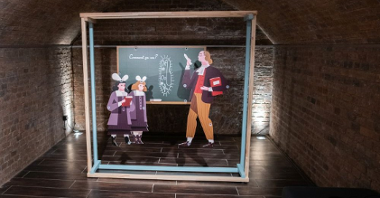 Ekspozycja złożona z wyciętych z papieru postaci nauczyciela i uczniów stojących przy szkolnej tablicy.