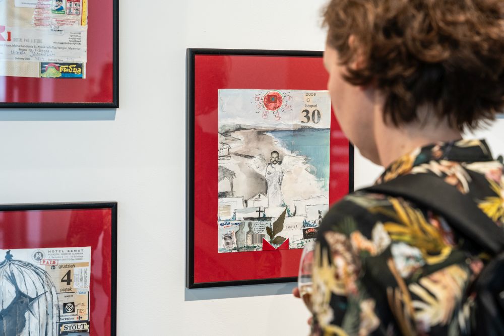 Stojąca tyłem do aparatu dziewczyna ogląda grafiki na ścianie galerii. To małe kolaże umieszczone w ramkach na czerwonym tle. - grafika artykułu