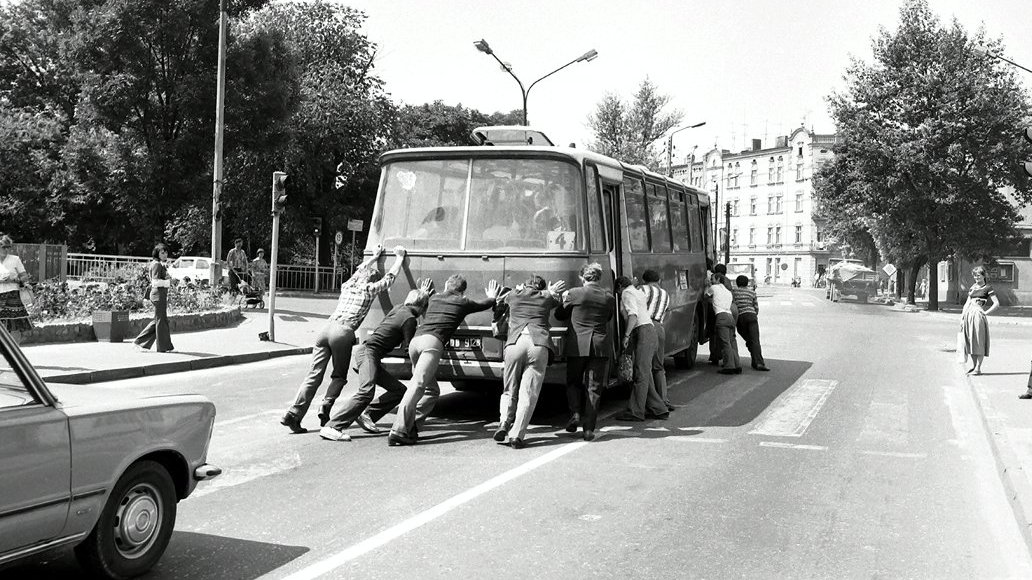 Ulica. Kilku mężczyzn pcha autobus.