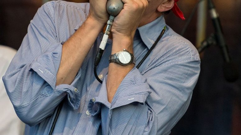 Frontman zespołu gra na harmonijce ustnej z zamkniętymi oczami.