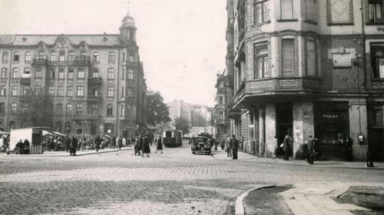 Czarno-białe zdjęcie ulicy, otoczonej kamienicami. Po lewej stronie widać rynek ze stoiskami. - grafika artykułu