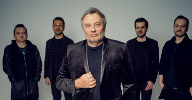 Krzysztof Cugowski jest ubrany w czarny garnitur z aksamitu, czarną koszulkę oraz spodnie. Za nim stoi czterech członków zespołu - wszyscy w czerni.