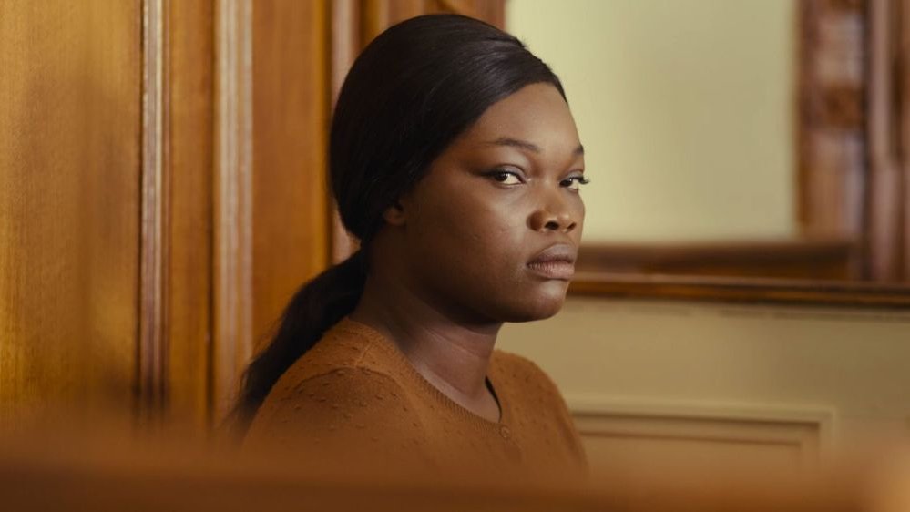 Czarnoskóra kobieta w ciasno upiętych włosach siedzi na ławie oskarżonych. Ma poważną minę, patrzy prosto w obiektyw.