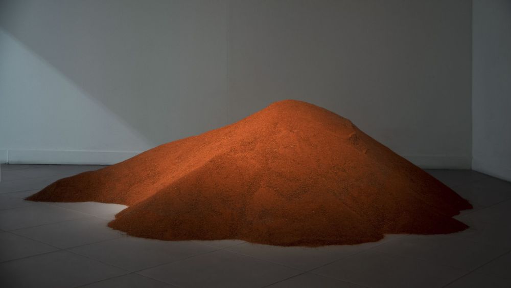 Sterta pomarańczowego piasku usypanego w galerii sztuki. - grafika artykułu