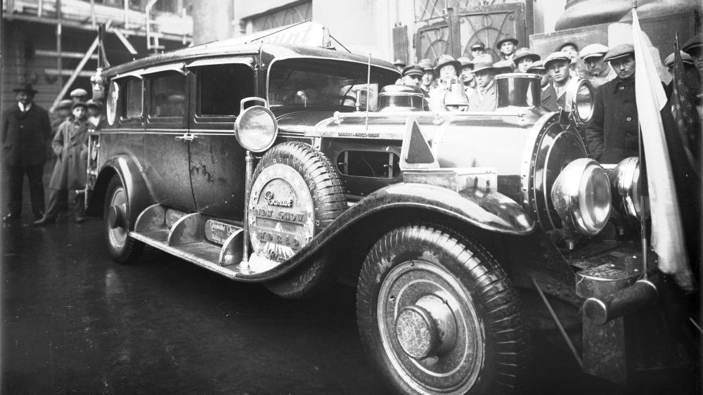 Czarno-białe zdjęcie starego samochodu. Dookoła pojazdu tłumy gapiów. - grafika artykułu