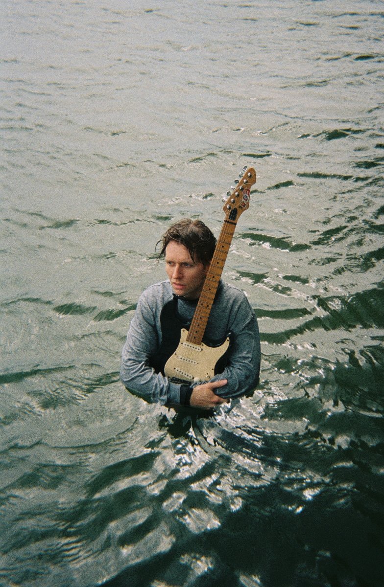 Mężczyzna trzyma gitarę i stoi do pasa w wodzie. - grafika artykułu