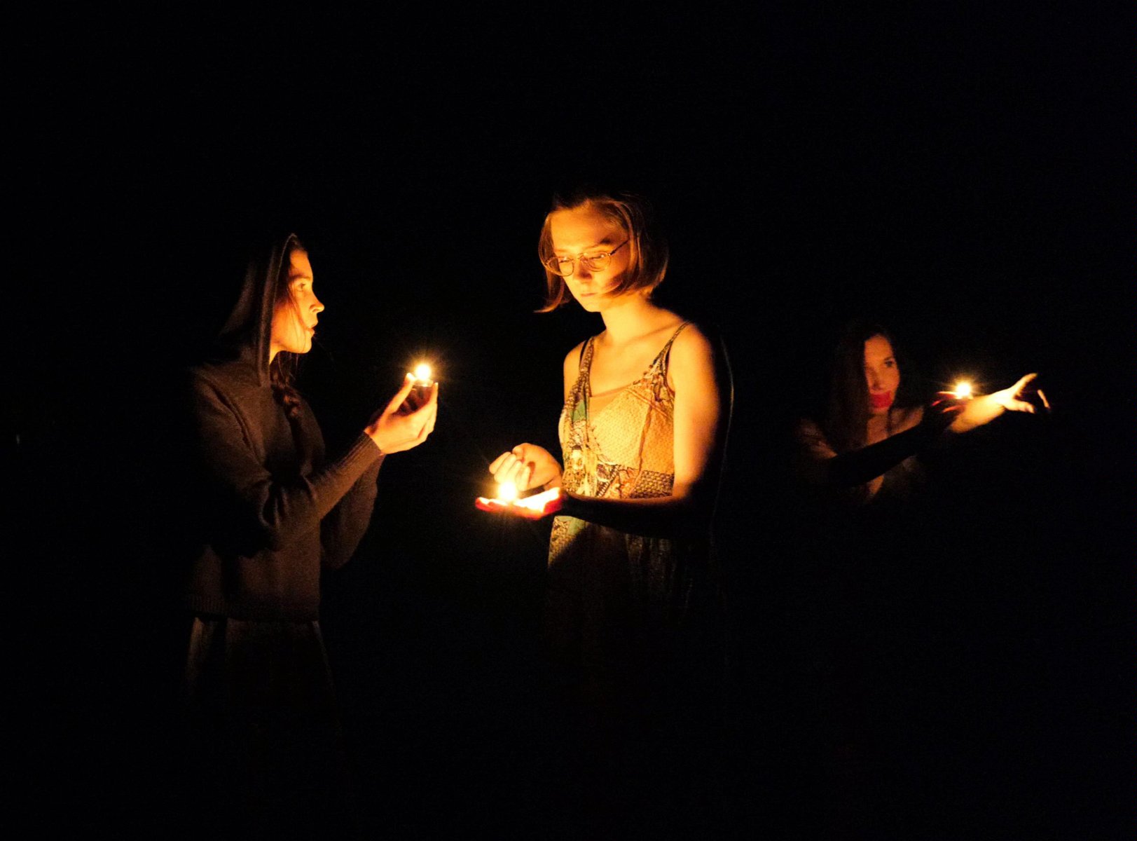 Trzy młode kobiety w ciemności zapalają zapałki, które oświetlają ich twarze. Każda patrzy w innym kierunku. - grafika artykułu