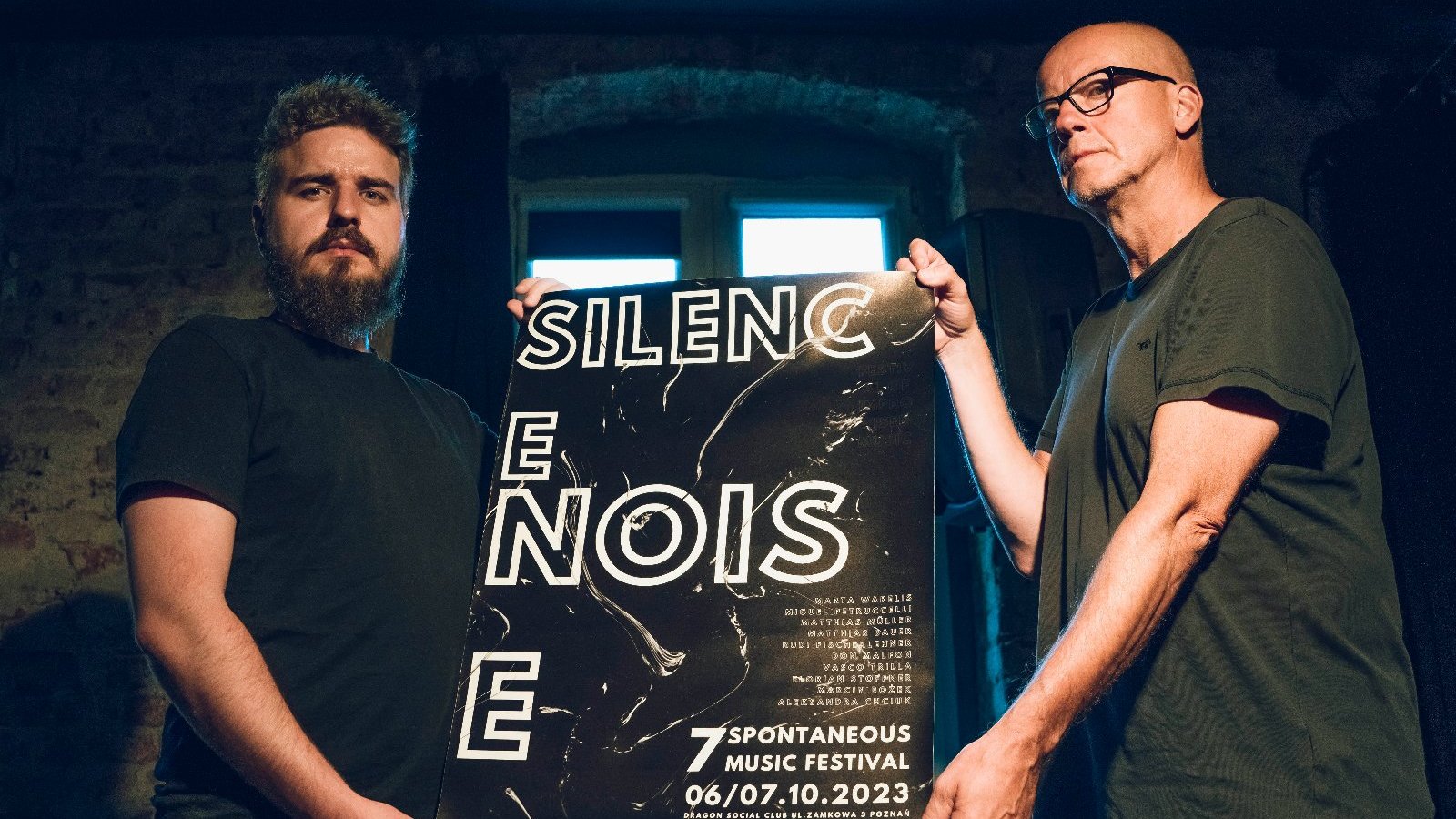 Dwóch mężczyzn trzyma plakat reklamujący festiwal z napisem "Silence. Noise".