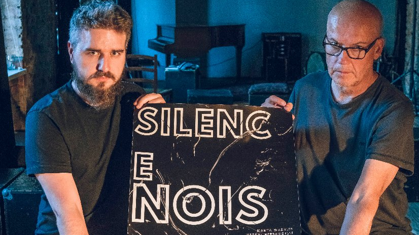 Dwóch mężczyzn trzyma plakat reklamujący festiwal z napisem "Silence. Noise".