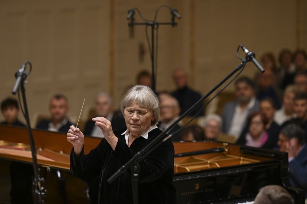 Agnieszka Duczmal dyryguje orkiestrą, ma zamknięte oczy. Za nią zasłuchana publiczność. - grafika artykułu