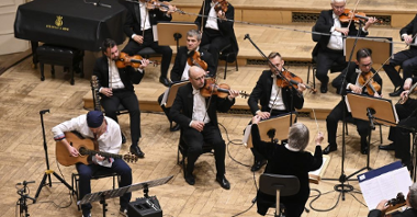 Orkiestra na scenie, z lewej gitarzysta Adam Palma pochylony nad instrumentem.
