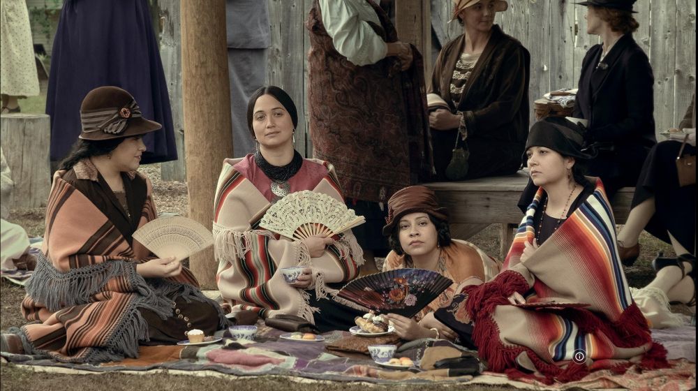 Grupa rdzennych Amerykanek siedzi w kręgu, część z nich nosi elementy europejskiego stroju. - grafika artykułu