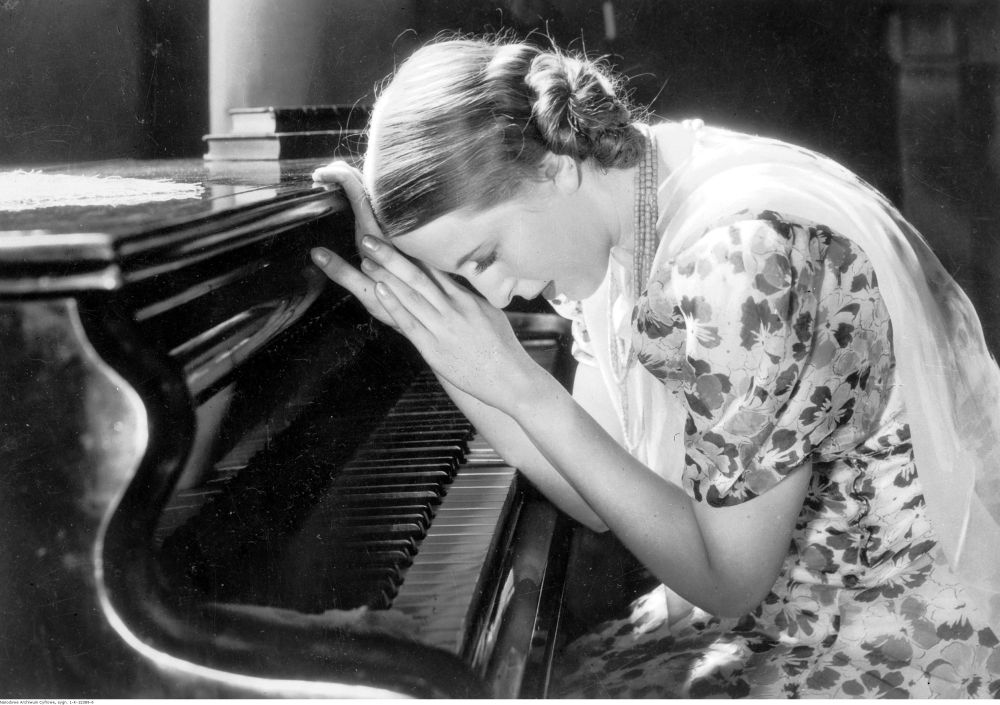 Czarno-biały kadr filmowy. Kobieta opiera się o wieko fortepianu. - grafika artykułu