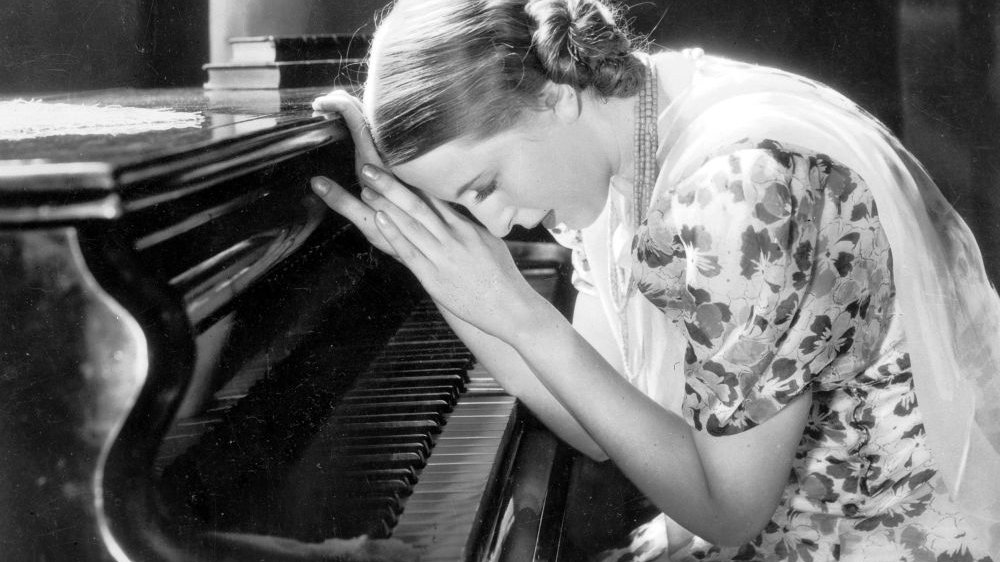 Czarno-biały kadr filmowy. Kobieta opiera się o wieko fortepianu. - grafika artykułu