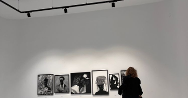 Kobieta ogląda prace wiszące na ścianie, stoi tyłem do fotografa.