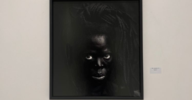 Czarno-biały portret czarnoskórej kobiety w dredach, patrzy prosto w obiektyw.