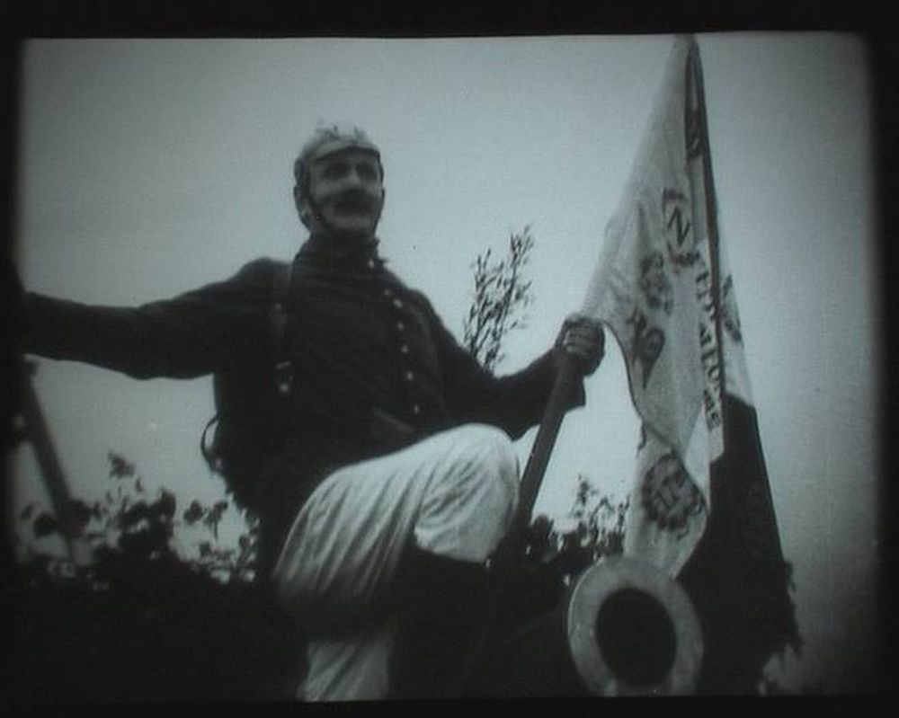 Czarno-biała stopklatka filmu przedstawiająca żołnierza w hełmie trzymającego w ręku flagę. - grafika artykułu