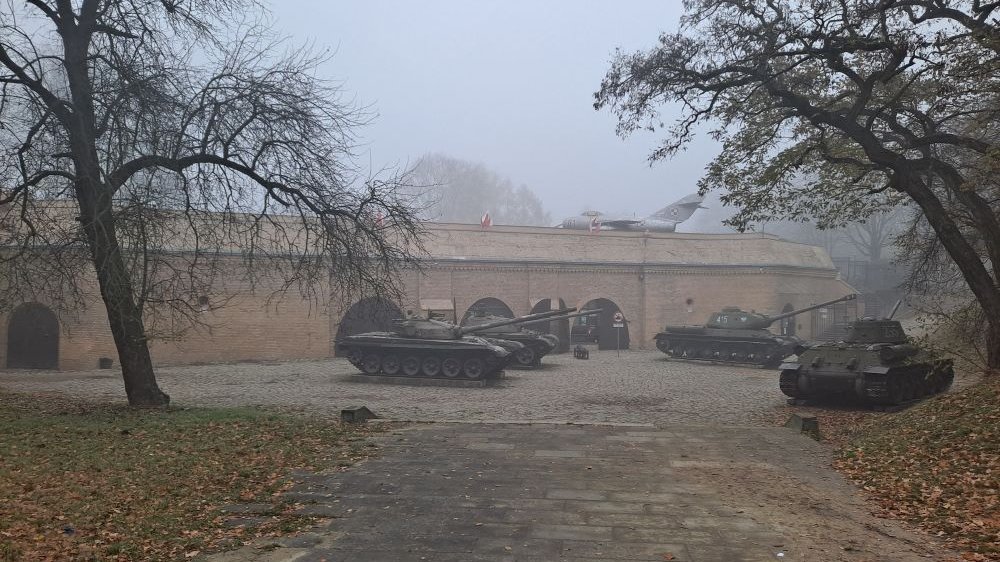 Mglisty jesienny dzień, w oddali widać zabytkowe czołgi, za nimi ceglany mur. - grafika artykułu