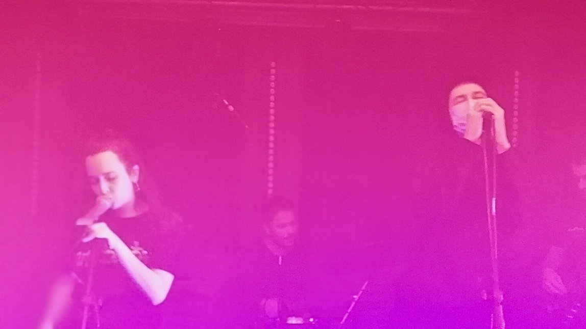 Wokalistka i wokalistka przy mikrofonach w klubie, w lekko zadymionej atomosferze, za nimi perkusita i basista - grafika artykułu