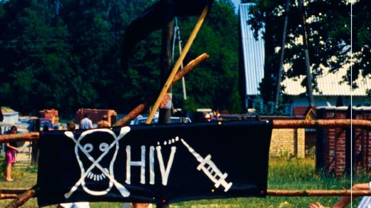 Okładka, na której widać chłopców grających bestrosko w piłkę, na płocie wisi czarny plakat z napisem "HIV" oraz narysowaną czaszką i strzykawką. - grafika artykułu