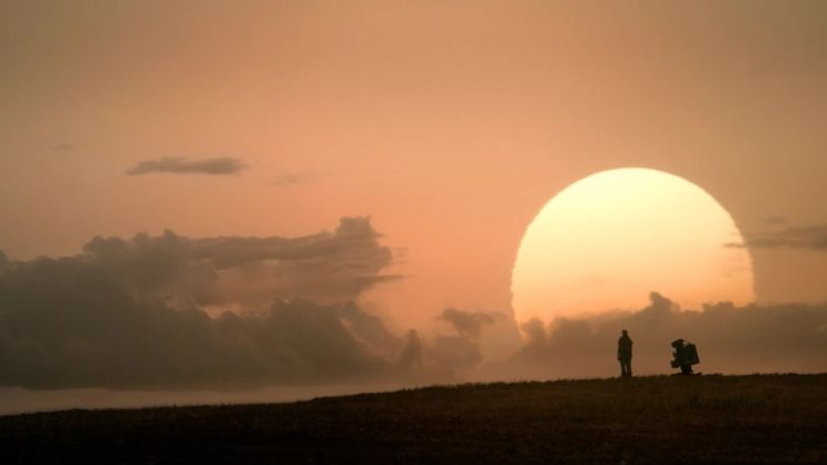 Zachód słońca, na jego tle horyzont z zarysowanymi postacią ludzką i robotem. - grafika artykułu