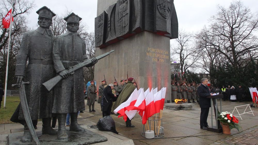 Uroczystości rocznicowe pod pomnikiem Powstańców Wielkopolkich. Mężczyzna przemawia do mikrofonu, dookoła niego żołnierze w historycznych mundurach.