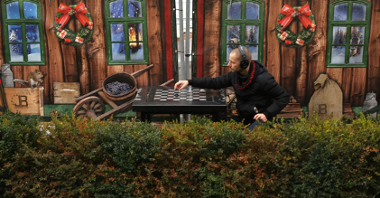 Mężczyzna w słuchawkach siedzi na świątecznym jarmarku przy stole do gry w szachy.