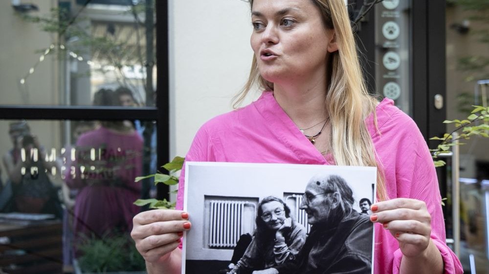 Kobieta w różowej sukience stoi przed kinem Muza. W rękach trzyma fotografię państwa Kalinowskich.