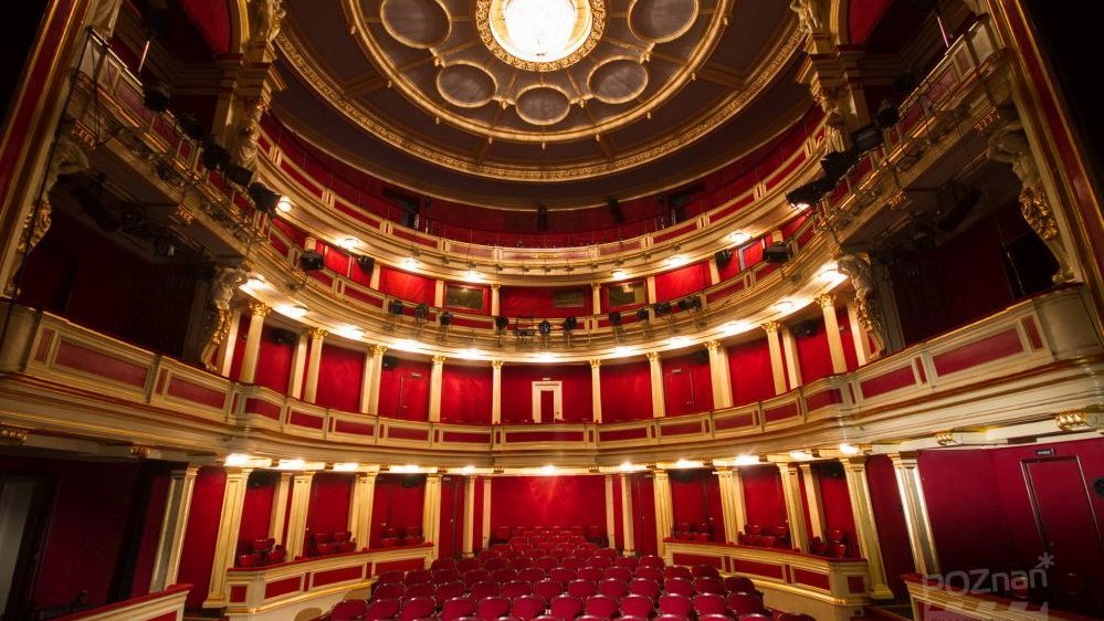 Puste wnętrze Teatru w kolorach czerwonym i złotym. Na suficie duży świecący żyrandol.