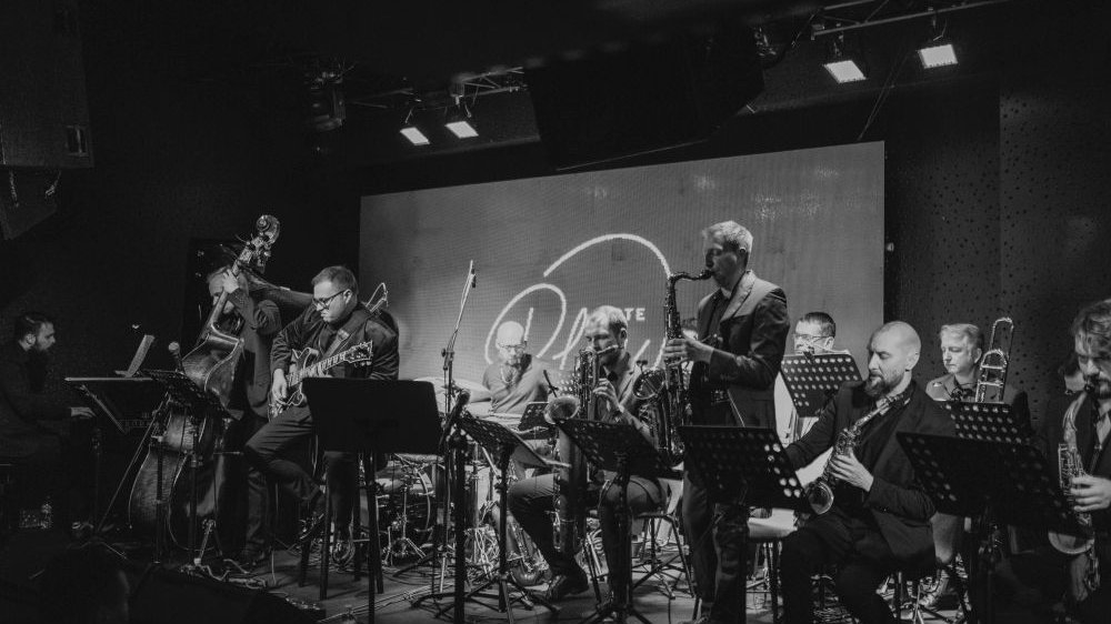 Czarno-białe zdjęcie orkiestry jazzowej na scenie klubu Blue Note.