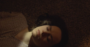 Kobieta leży na dywanie z zamkniętymi oczami, na jej twarz pada snop światła.