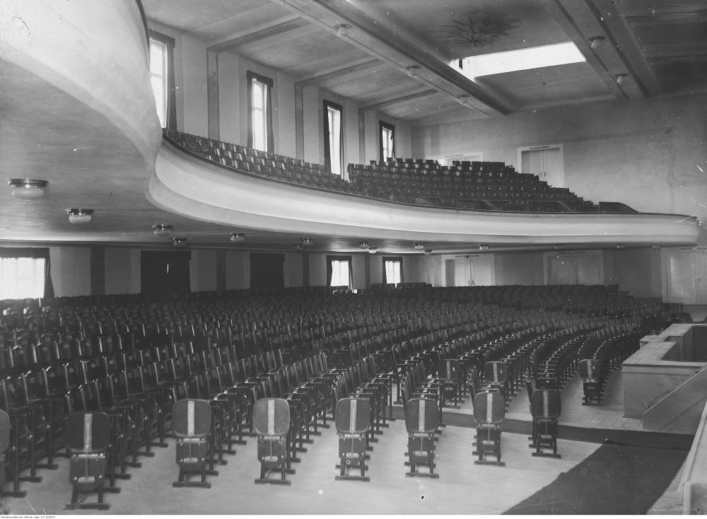 Czarno-białe zdjęcie sali kinowej z drewnianymi krzesłami na parterze i antresoli. - grafika artykułu