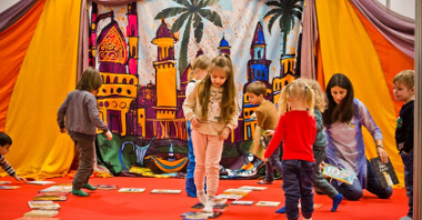 Dzieci bawią się na tle rozpiętej, kolorowej tkaniny, na której namalowano bajkowy zamek.