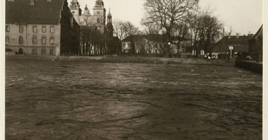 Widok na katedrę poznańską i okoliczne budynki znad brzegu rwącej Warty.