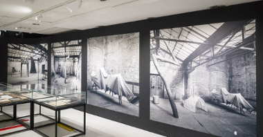 Czarno-białe, wielkoformatowe zdjęcia na ścianach, po lewej szklane gabloty.