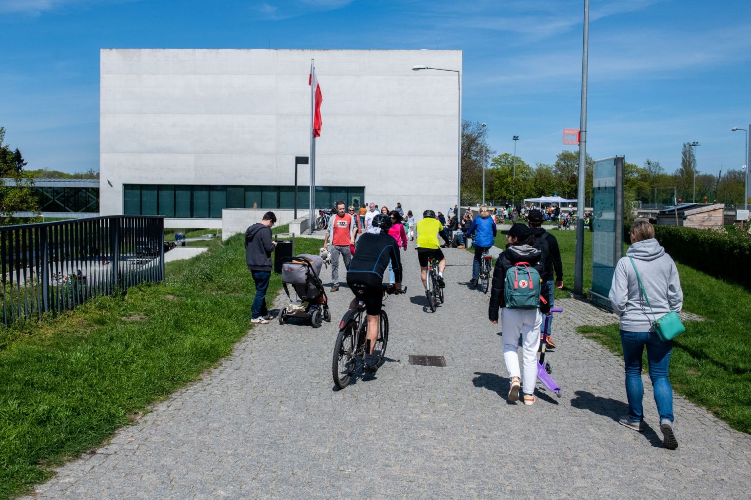 Rowerzyści, ojciec z dzieckiem w wózku i spacerowicze zmierzają w stronę Bramy Poznania - grafika artykułu