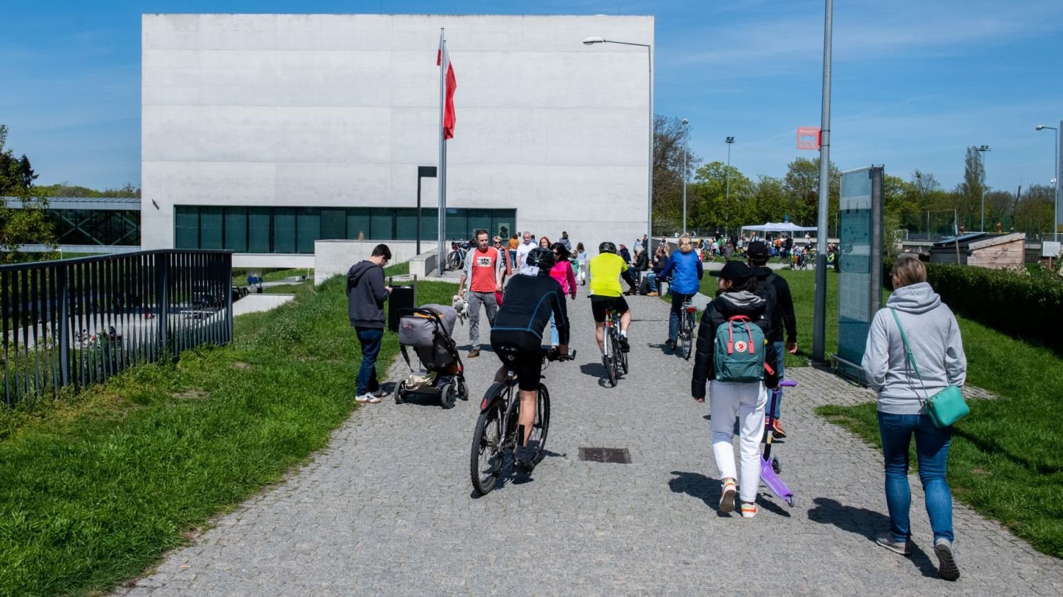Rowerzyści, ojciec z dzieckiem w wózku i spacerowicze zmierzają w stronę Bramy Poznania