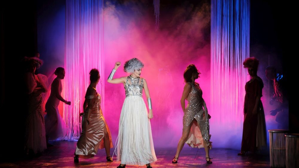 Atena tańczy na środku, wokół niej pozostałe boginie, scena jest pokrywa różową mgłą, a Atena ma bojowy wyraz twarzy.