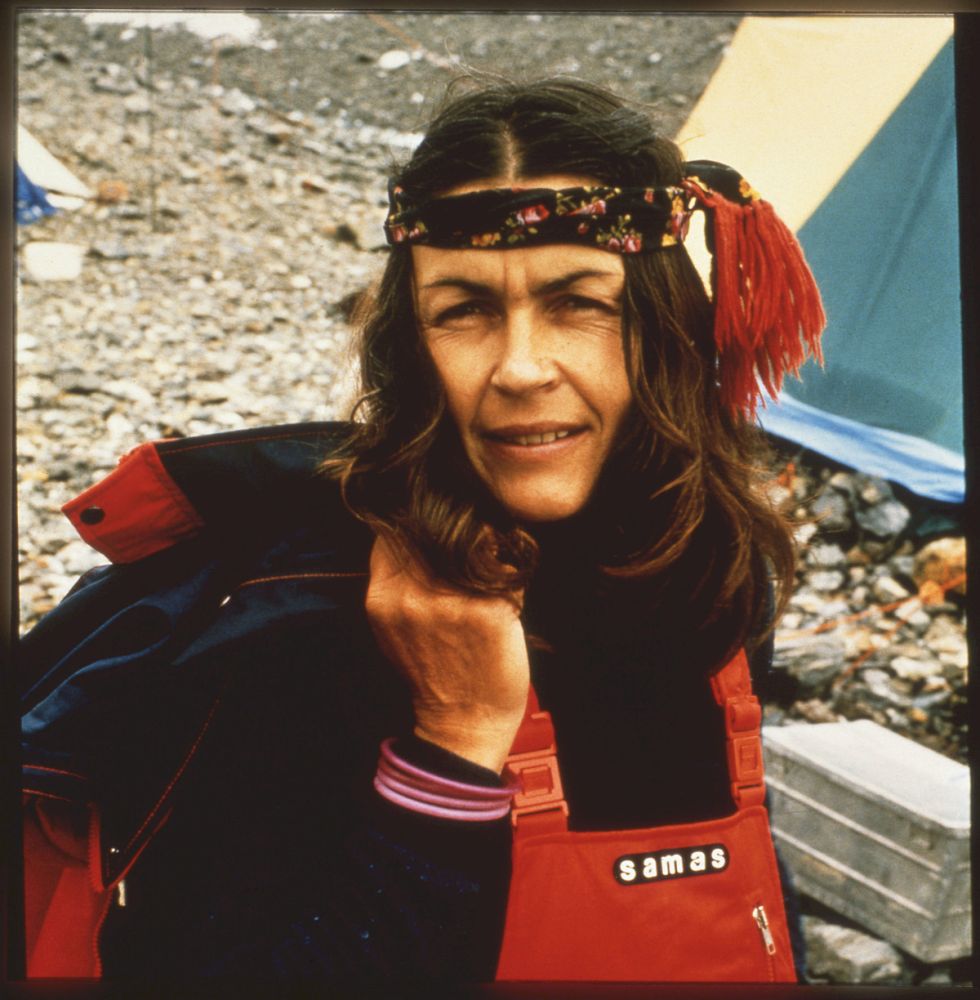 Wanda Rutkiewicz w górskim stroju i chuście z frędzlami na głowie pozuje na tle rozbitego namiotu pod zdobywanym szczytem. - grafika artykułu