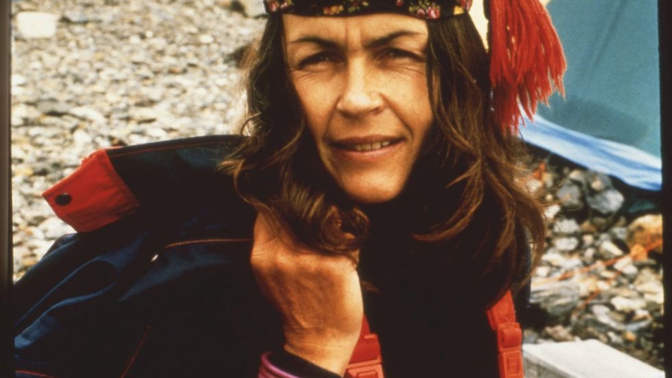 Wanda Rutkiewicz w górskim stroju i chuście z frędzlami na głowie pozuje na tle rozbitego namiotu pod zdobywanym szczytem.
