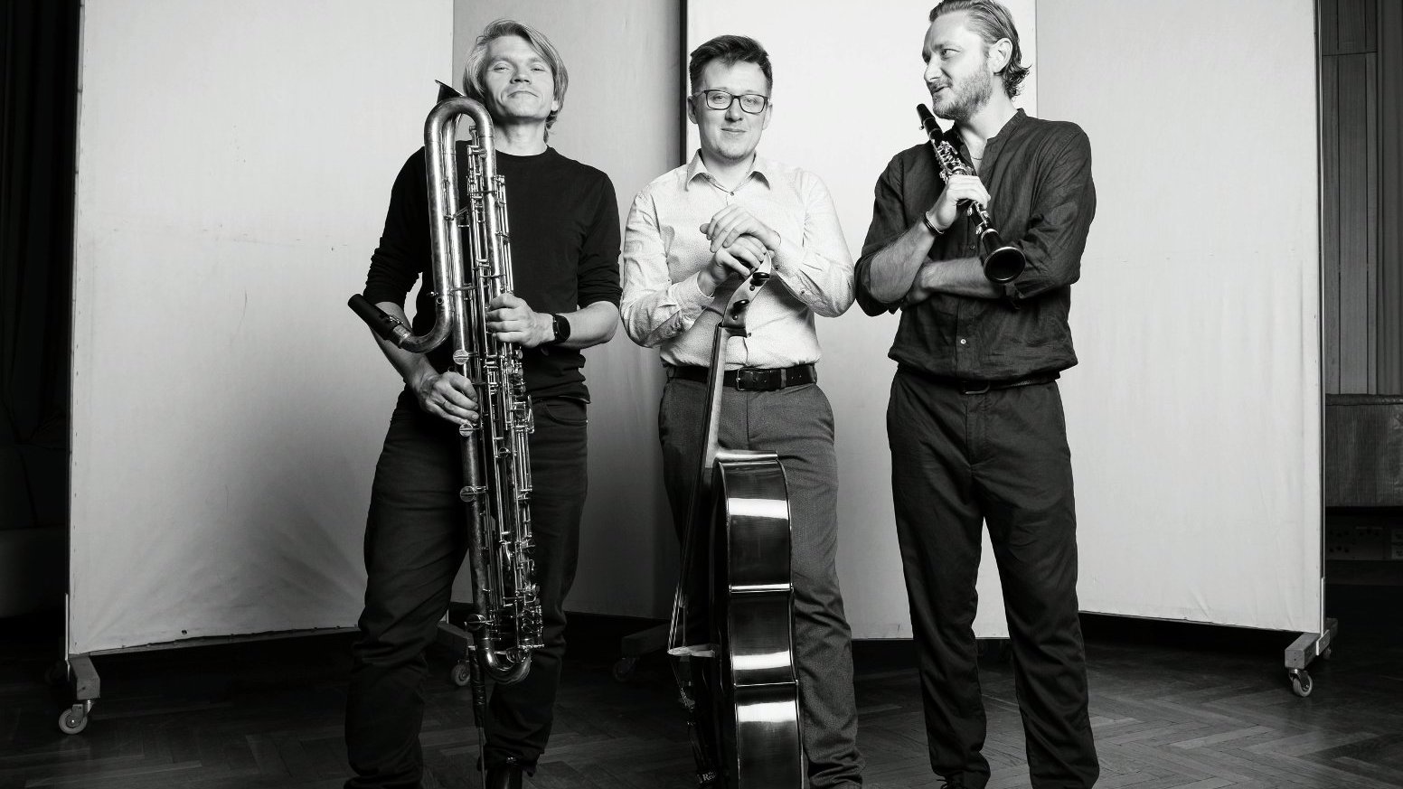 Trzech mężczyzn stoi z instrumentami muzycznymi: klarnetem kontrabasowym, wiolonczelą, klarnetem