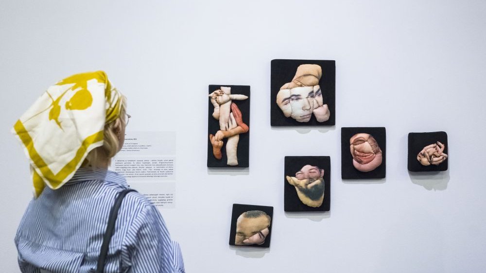 Małe obrazki na wystawie przedstawiają uszyte z materiałów poduszki, które wyglądają jak fragmenty ludzkich twarzy lub ciał.