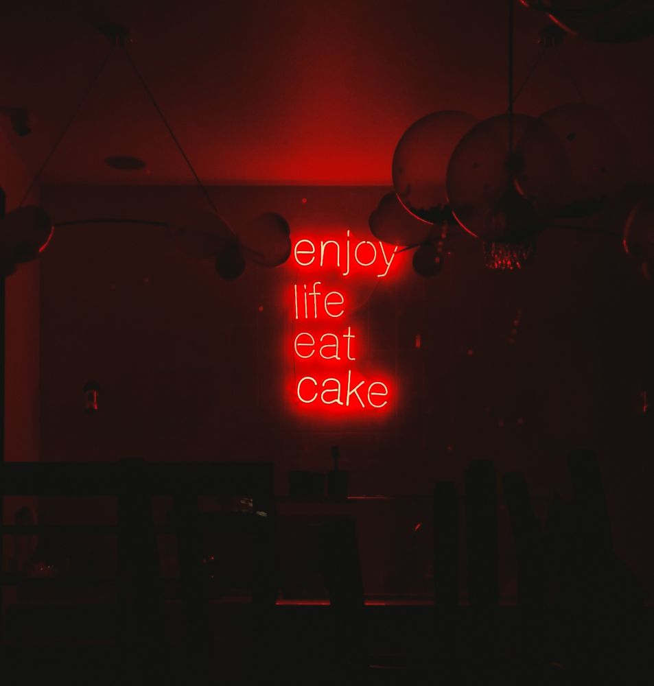 Świecący na czerwono neon-napis "Enjoy life eat cake". - grafika artykułu