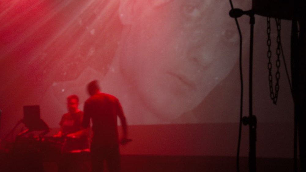 Scena, czerwone światło, dym. Na ekranie wyświetlone zdjęcie twarzy kobiety.