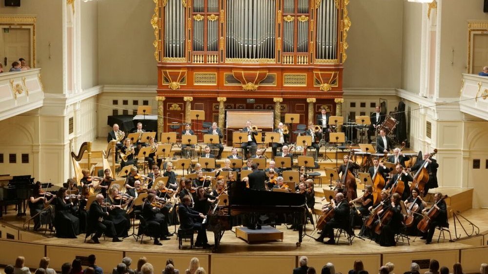 Sala Filharmonii Poznańskiej, na środku stoją ogromne, bogato zdobione i złocone organy. Pod nimi jest scena, na której stoją muzycy.