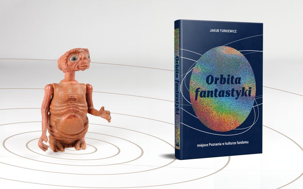 Książka z granatową okładką z motywem kosmosu. Obok niej pomarańczowa figurka kosmity wyglądającego jak filmowy E.T. - grafika artykułu