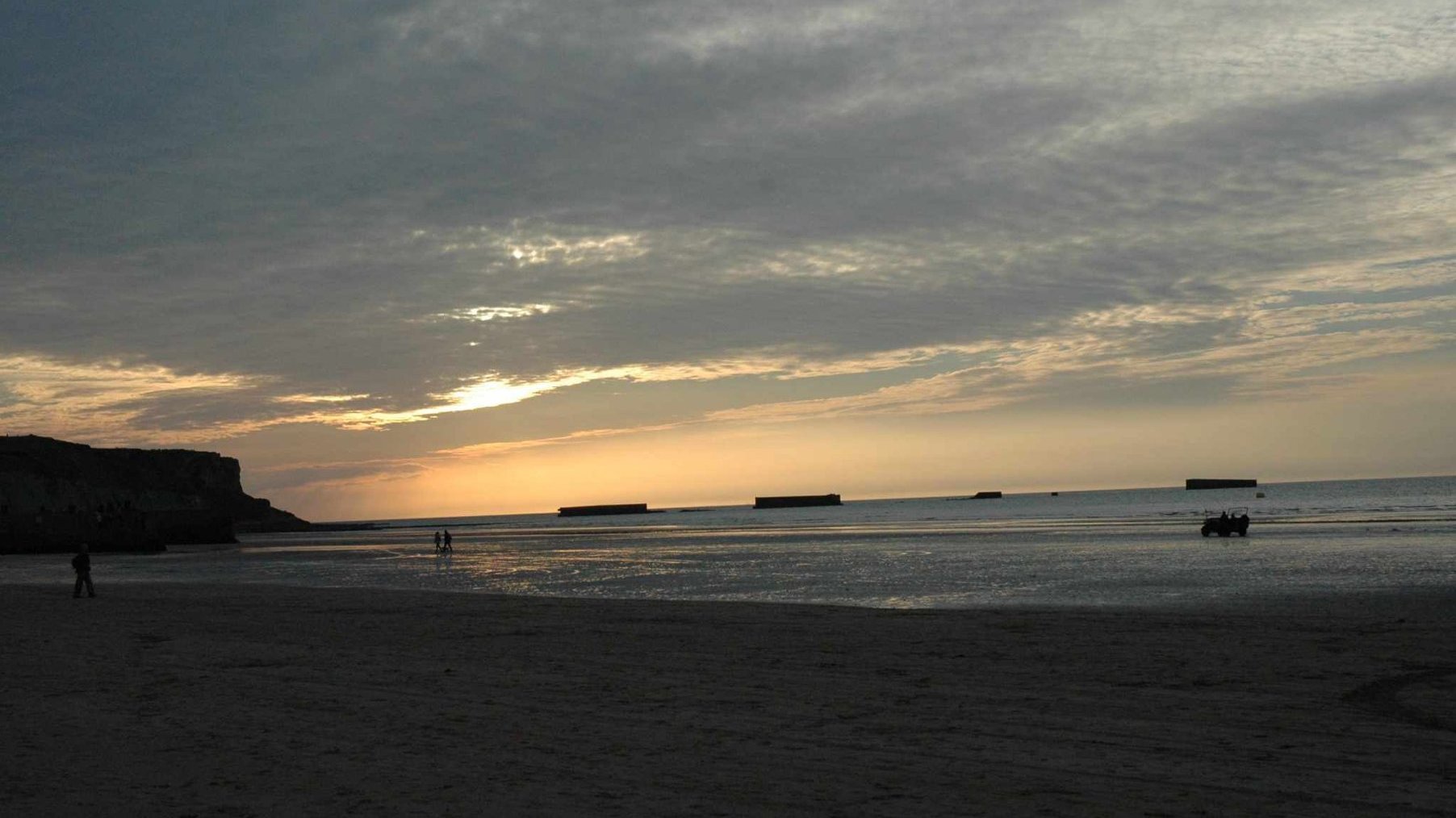Powierzchnia morza o zachodzie słońca, w oddali rozproszone prostokątne kształty - pontony.