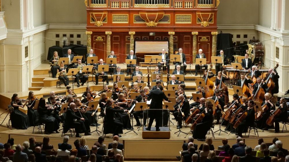 Muzycy filharmonii występują na scenie. Pod sceną publiczność, za sceną ogromne drewniane organy.