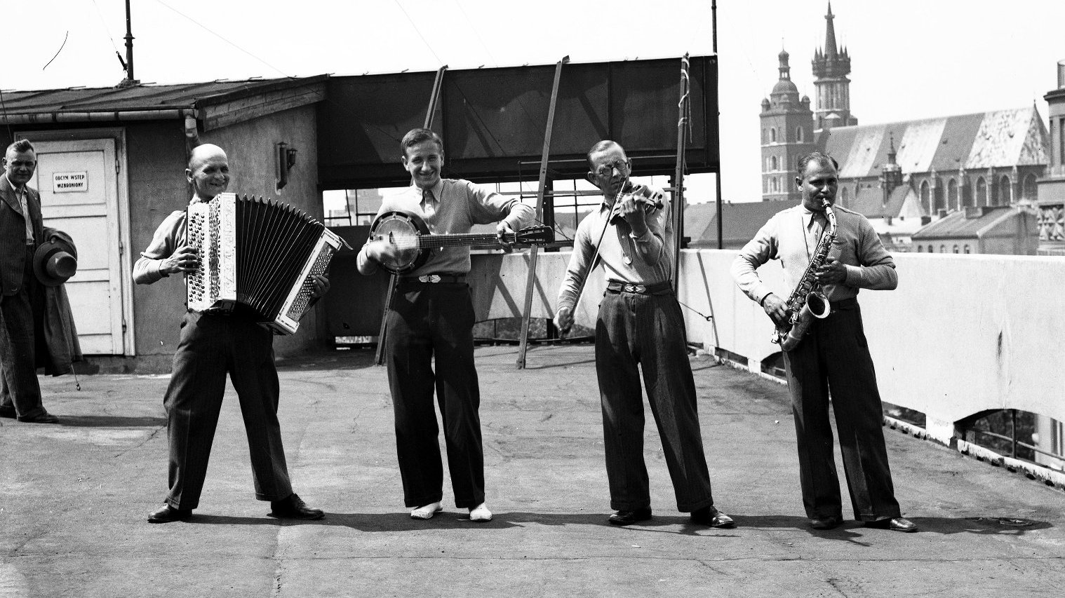W centrum czarno-białej fotografii jest czterech mężczyzn w średnum wieku z instrumentami muzycznymi. Mają eleganckie spodnie i koszule. Są w dobrym nastroju.
