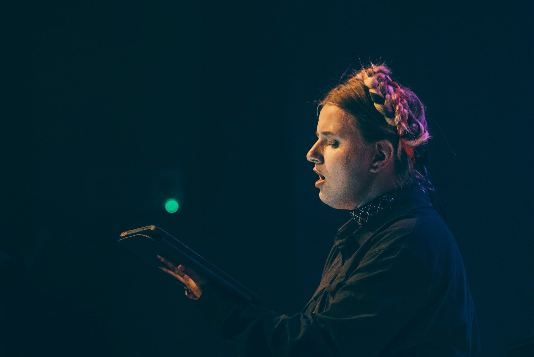 Członikini Chóru Skovoroda: śpiewająca młoda kobieta z warkoczem na głowie. W ręku trzyma tablet. - grafika artykułu